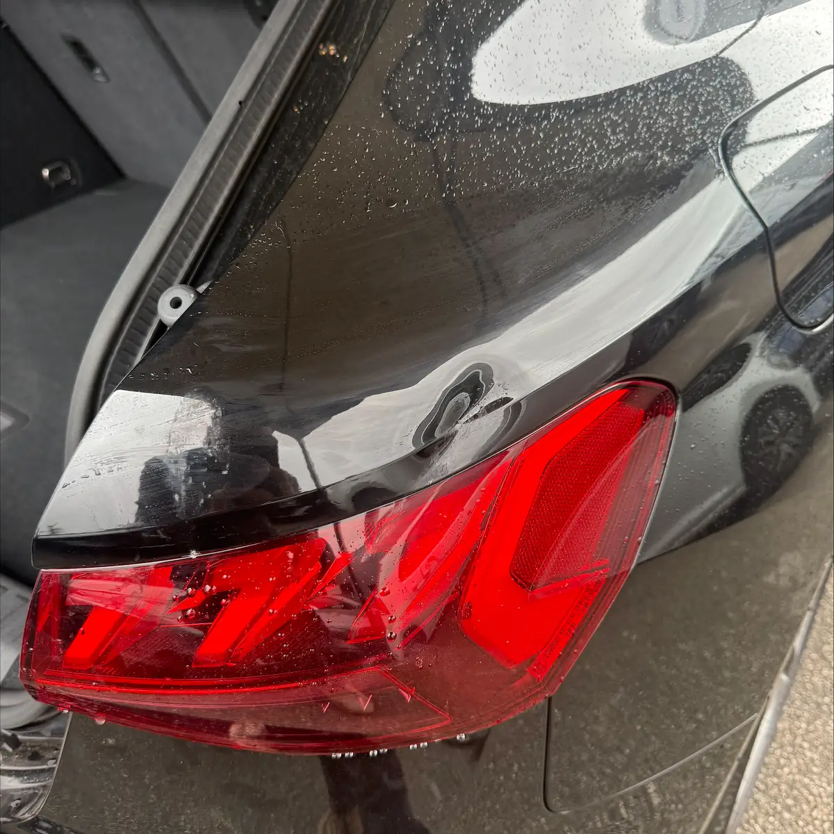 Black Audi rear quarter panel with a dent above the rear light, before repair